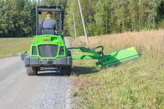 Loader with a flail arm attached to a mower cutting an angled hill. #mower #landscaping #loader #tractor #cuttinggrass #ridinglawnmower #forest #treecare #tree #tallgrass #worksmarternotharder