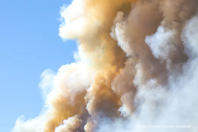 Plumes of smoke rise against a blue sky.