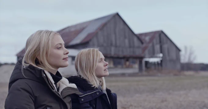 Sarah Gadon and Alison Pill look out at a farm field with two barns behind them