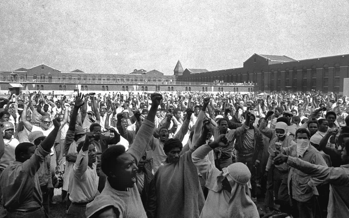 Prison inmates at Attica raise their fists in the air in this black and white photo