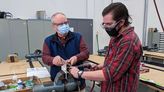 An STLCC student in the Boeing pre-employment training program practices riveting on sheet metal as his professor looks on.