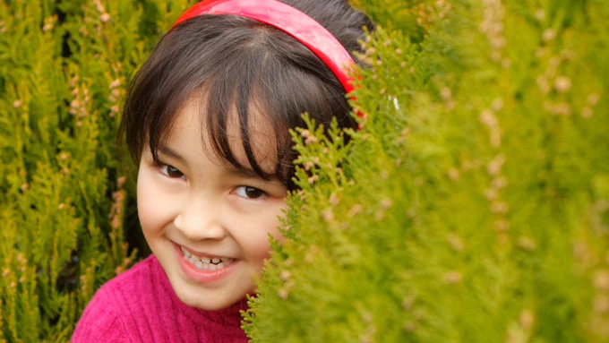 Girl peeping behind a small tree as she plays a game of hide and seek