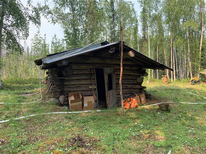 A small log cabin in the woods is surrounded by fire hose and fire protection equipment.