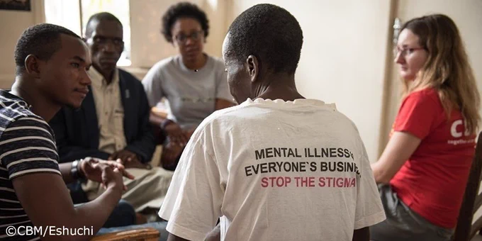 People in Malawi having a conversation about mental illness. One man's t-shirt reads "Mental illness, everyone's business, stop the stigma"