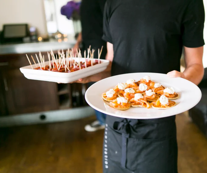 Waiter holding cocktail food on plates.