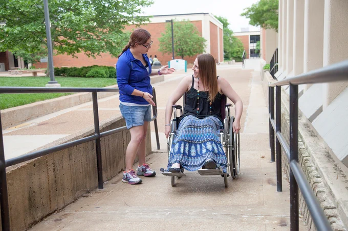 A female student in a wheelchair works her way up a ramp on the STLCC-Meramec campus as a another female student talks to her