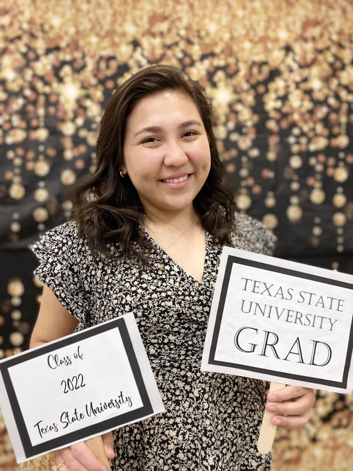 Student posing in front of black and gold glittery backdrop with graduation signs