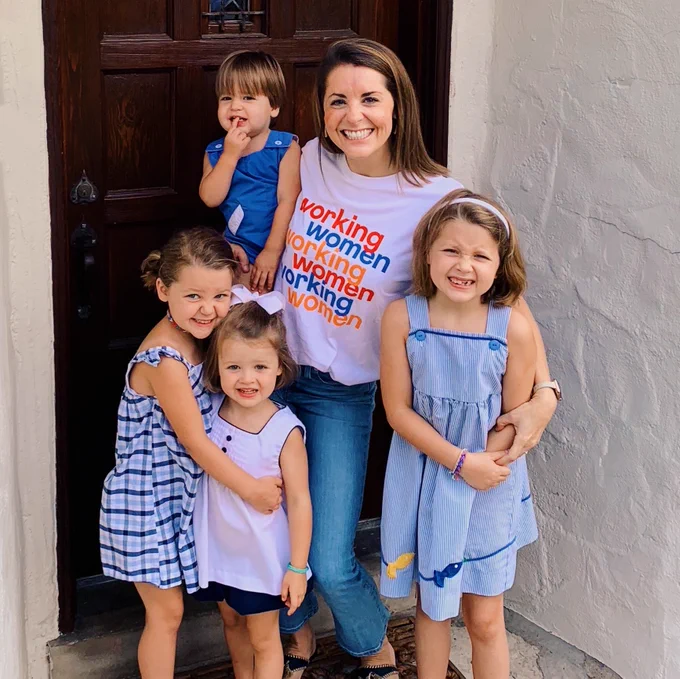 Photo of Inclusively's COO Sarah Bernard, a woman with brown hair is standing in her doorway with her four young children. Sarah is wearing a white #Argent t-shirt with the words displayed three times, working women, working women, working women.