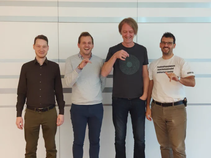 Showing the four hosts of @DevMelange standing in a line smiling, and attempting to do a hand motion of drinking coffee