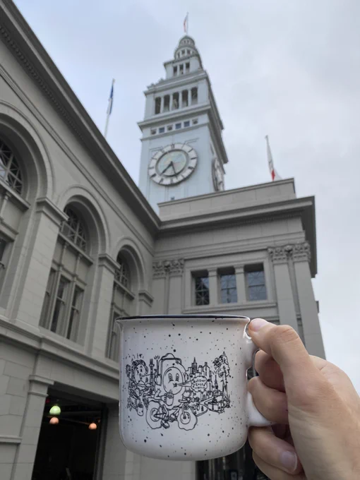 I’m the foreground a Roll Over Easy mug depicting an egg riding a bicycle around San Francisco, and in the background the clock atop the Ferry Building
