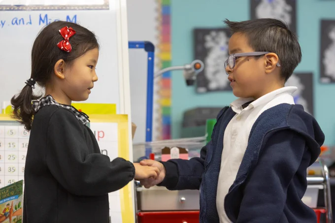 Two kindergarten students shake hands in front of an easel