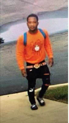 surveillance camera still shot of man in dark pants, orange shirt