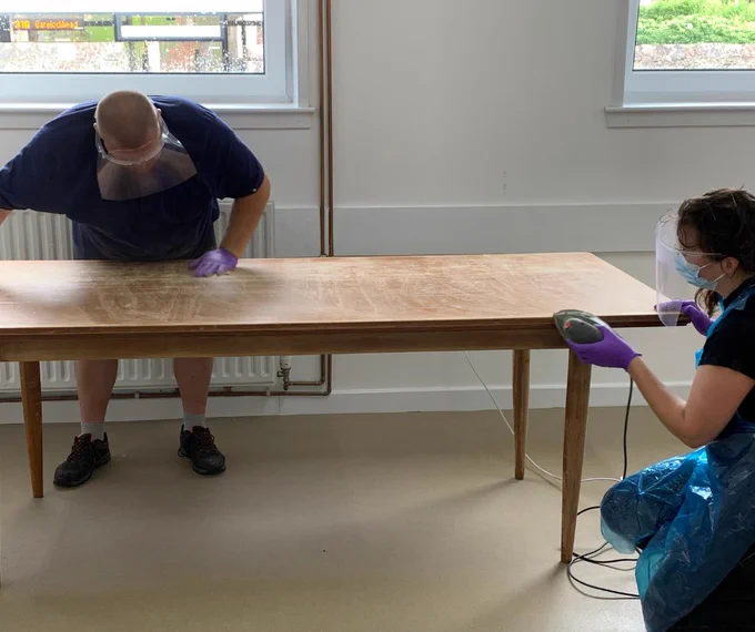 Man and woman sanding a dining table in preparation for an upcycling project.