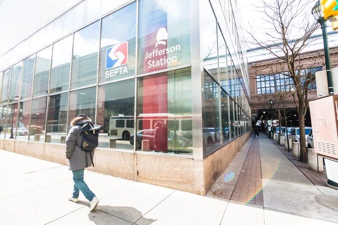A person in jeans and a winter jacket walking by SEPTA's Jefferson station in Philadelphia during the day.