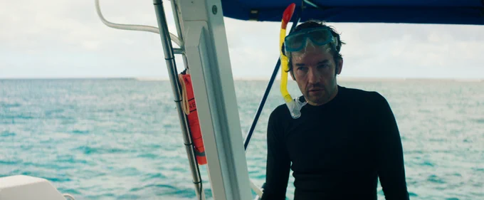 A close-up of Nash Edgerton in a black swimsuit and scuba gear sits on a boat at sea.