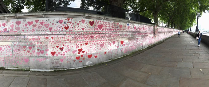 Panoramic photo showing long wall by side of the Thames, covered in hearts.