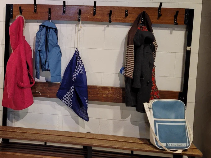 Wooden bench and hooks with children's coats, bags and and a PE kit bag.