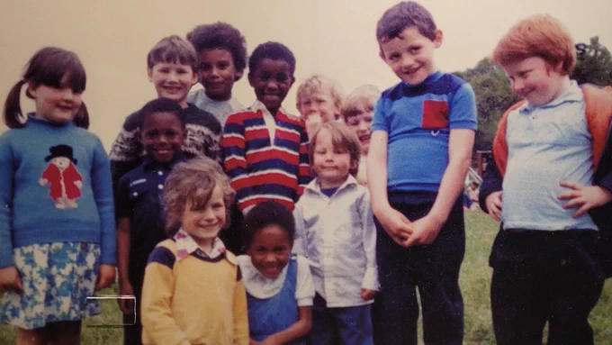 Group of children, possibly on a school trip, huddled together and smiling to camera.