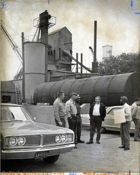 Six people stand in parking lot of asphalt plant