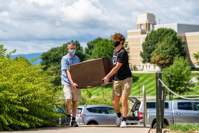 Student and parent carry minifridge towards East Campus dorm.