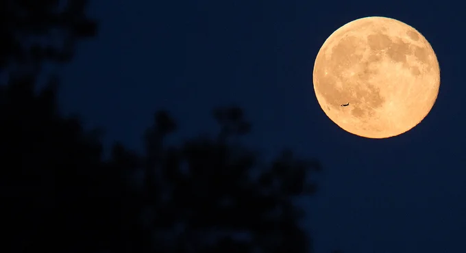 Full moon in night sky with aircraft passing in front