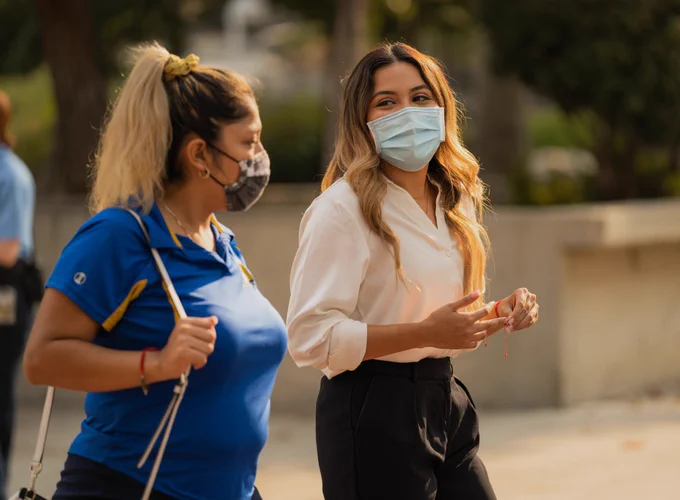 Two women walking outside wearing face masks. 