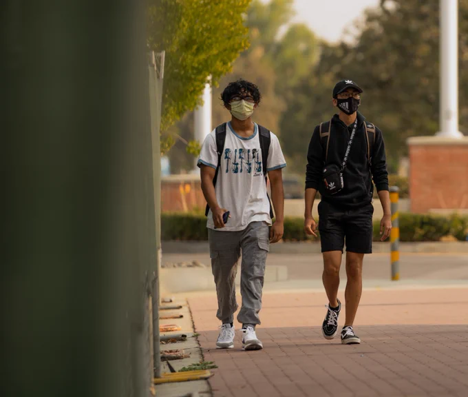 Distance photo of two men walking with face masks on. 