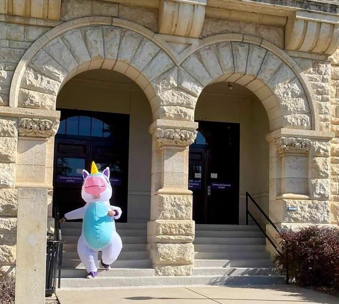 Dr. Haddock wearing an inflatable unicorn costume walking down the front steps of Holton Hall.