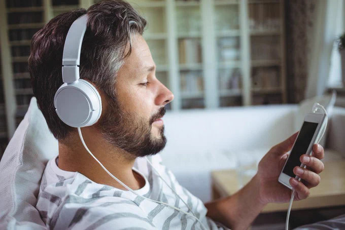 Male wears headphones while watching something on smartphone