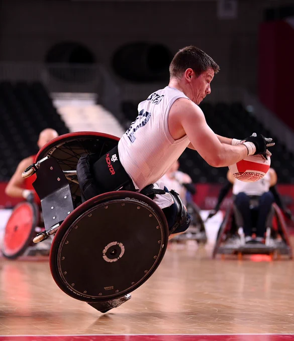 Player tips in wheelchair grabbing the rugby ball