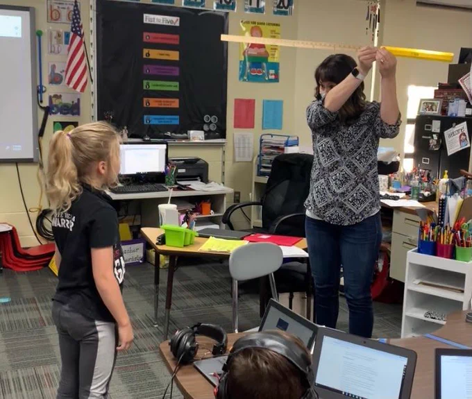 Teacher holding up ruler as student stands near by and looks at her.