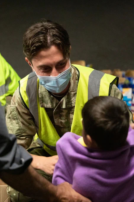 Male soldier speaks to a child wrapped in a blanket