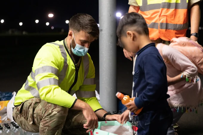 Male soldier hands out a bottled drink to a boy.