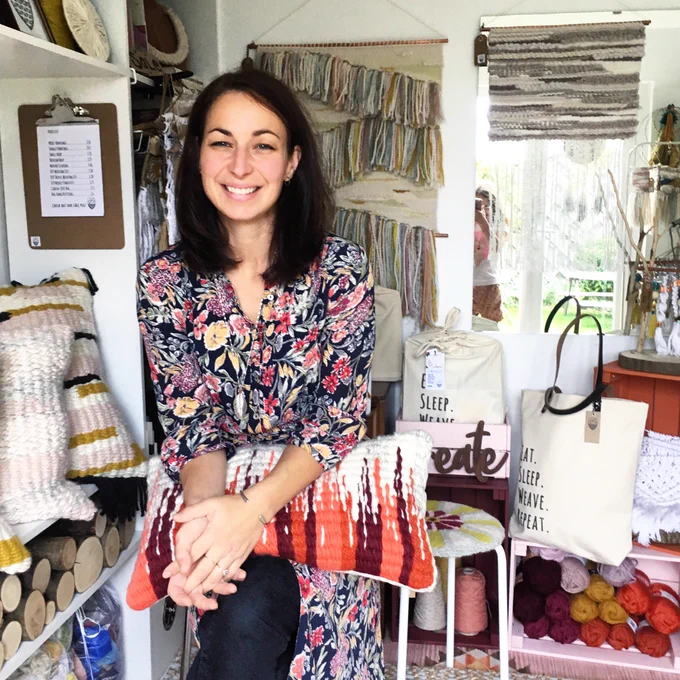 Stephanie Fradette smiling in studio surrounded by woven textiles