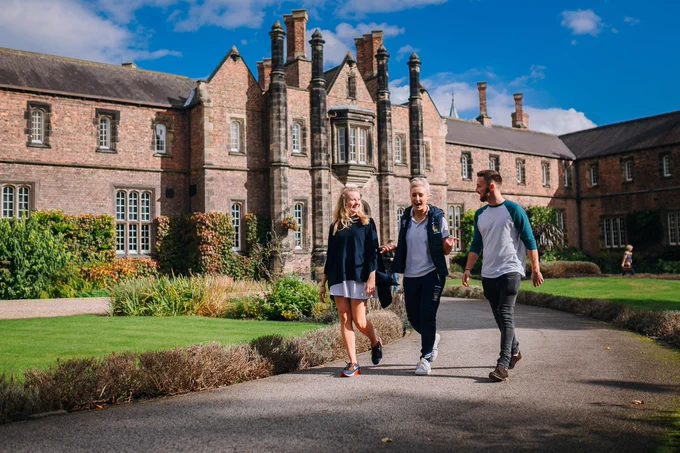 Three students walk in front of the York St John campus in the sun