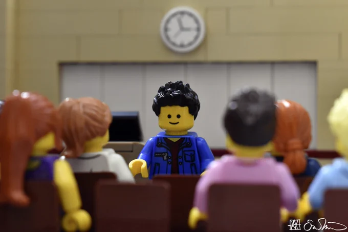 LGS stands in front of a class of students. He blankly looks down at the ground.