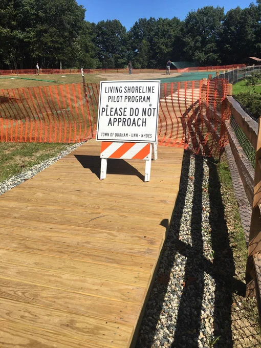 Image of caution sign along a wooden boardwalk in front of newly planted grassy area.