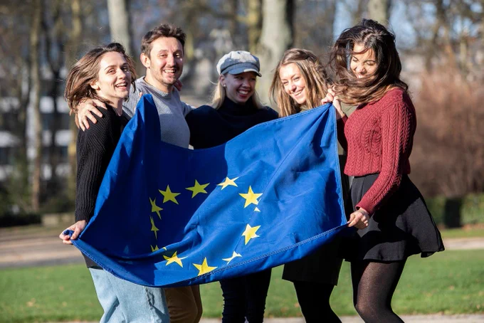 Five people holding the EU flag together in the park