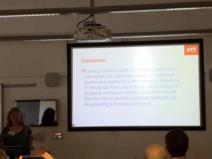 person giving talk with powerpoint slide in the background on 'conclusions'