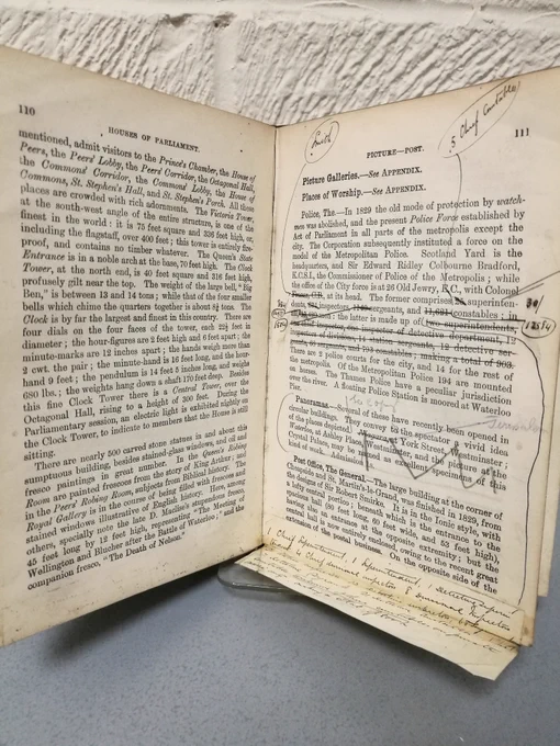 Photo of pages from the 'Illustrated Guide to London'. There are sections of the text crossed out, and notes written in the margins and glued in at the bottom of the page.