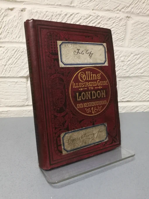 Photo of 'Collins' Illustrated Guide to London and Neighbourhood'. The cover is red leather with the title picked out in gold in a circle. A sticker on the cover reads 'File copy'.