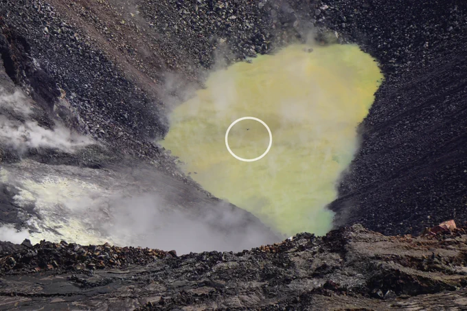 Unmanned aircraft system carrying a container for water over a pond in a volcanic crater