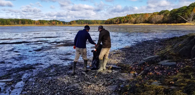 Image of two people collecting trash on a rocky shoreline of an estuary.