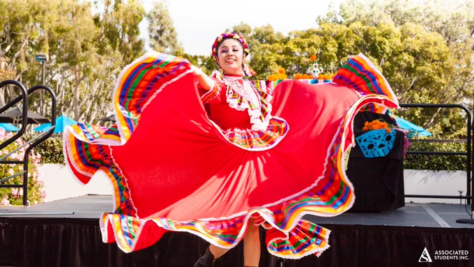 A young woman in a bright red dress trimmed with yellow, black and green dances on a stage. 