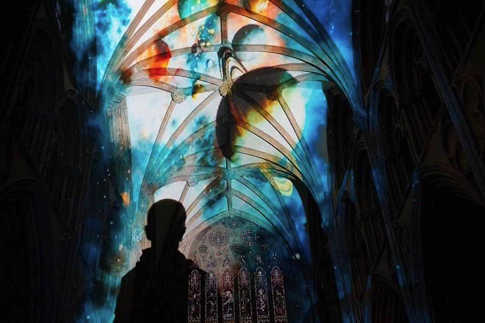 A child looks up at a cathedral ceiling lit up with colourful projections 