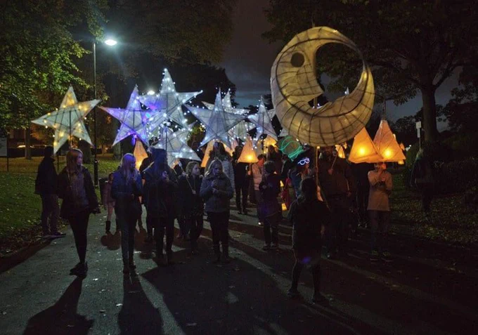 A group of people carrying enormous lanterns in the shapes of a moon and stars