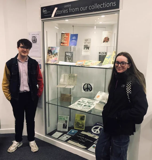 Young man and woman standing either side of display of archival materials