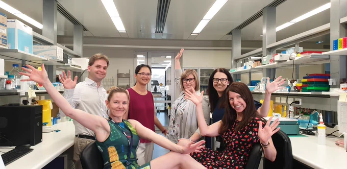 6 scientists wearing colourful clothing posing in a science lab