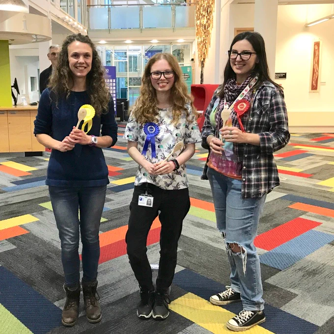 Emmeline, Sophie and Kelleigh standing proudly with their rosettes and spoons and Bake Your Research winners.