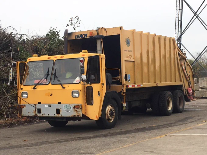 Image of yellow recycling truck driving on a road.